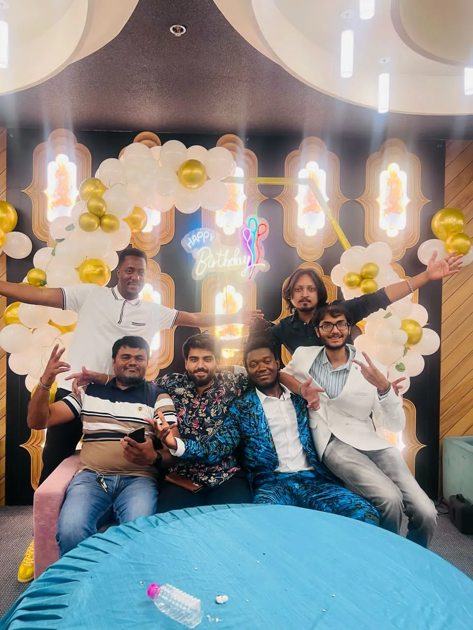 A playful group photograph beneath gold and white balloons at a birthday celebration.