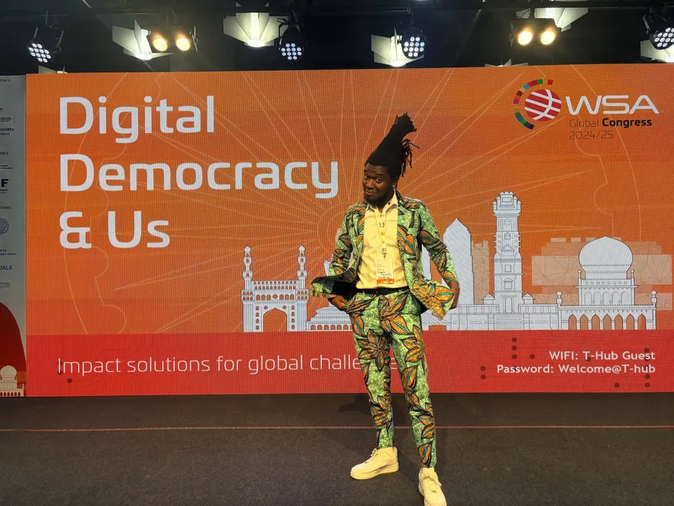 Joseph at the WSA Global Congress in front of the orange Digital Democracy & Us backdrop.